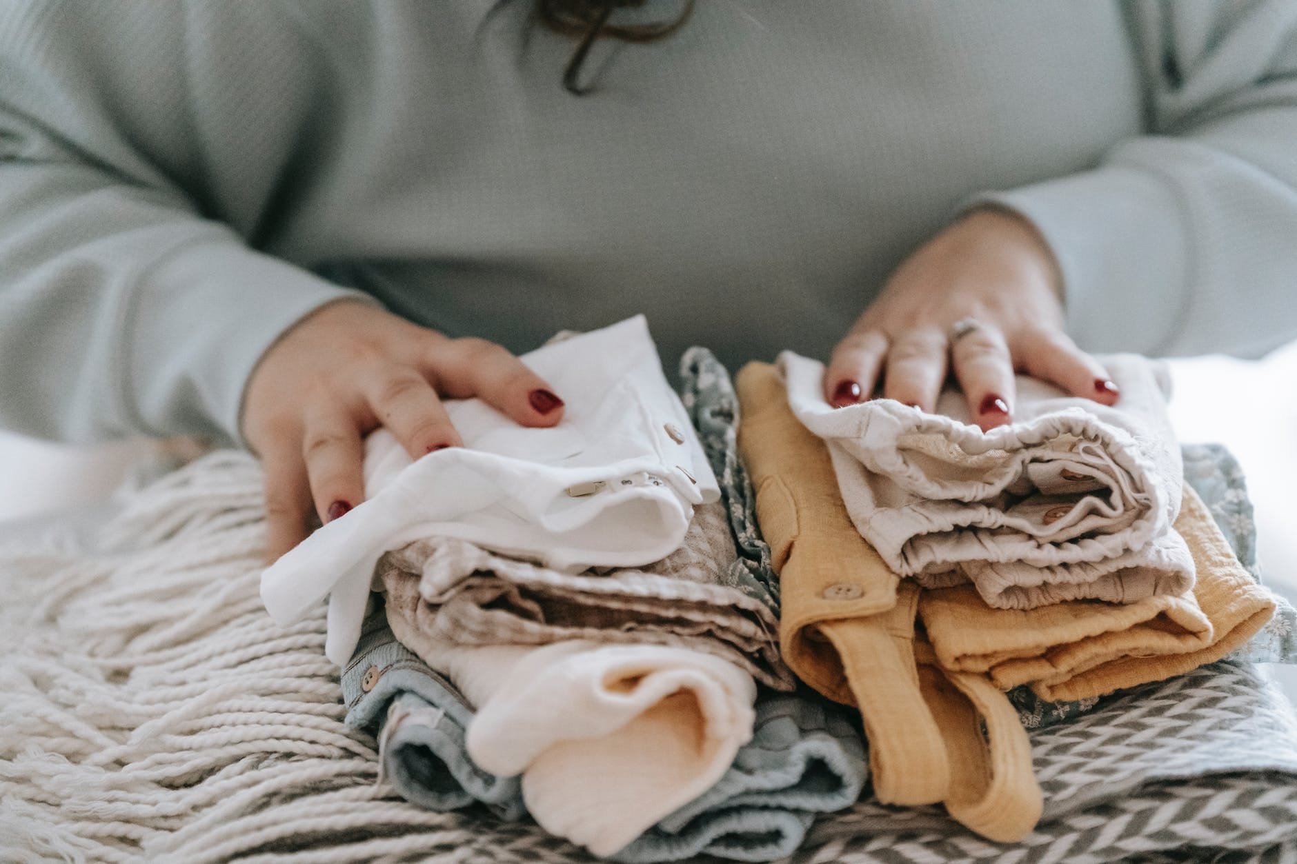 unrecognizable woman with folded clean baby clothes