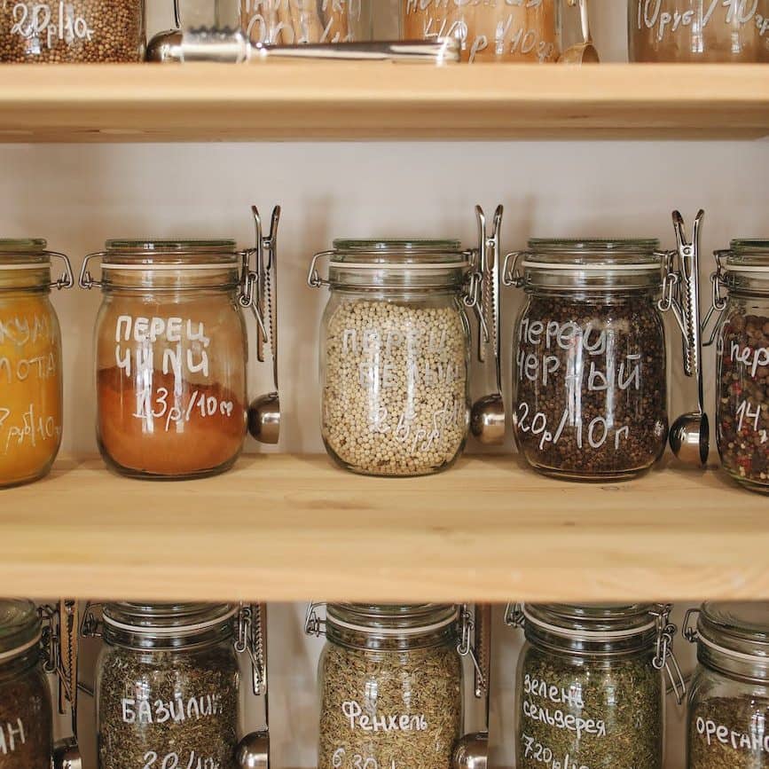 variety of spices in glass jars on wooden shelves